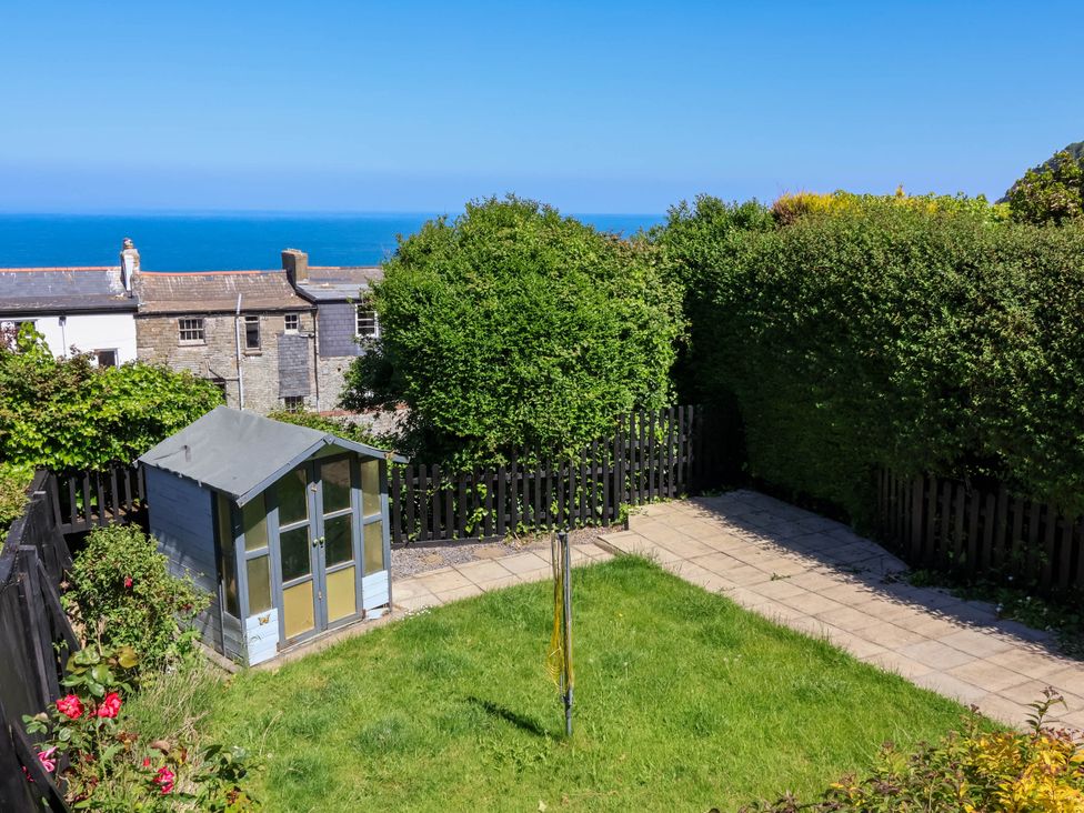 A garden with a small shed a paved walkway a rotary clothesline and hedges at Combe View in Ilfracombe