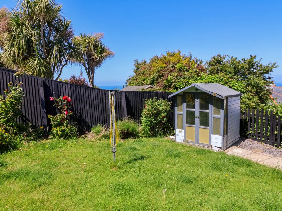 A garden with green grass a small shed a rotary clothesline and trees behind a black wooden fence at Combe View in Ilfracombe