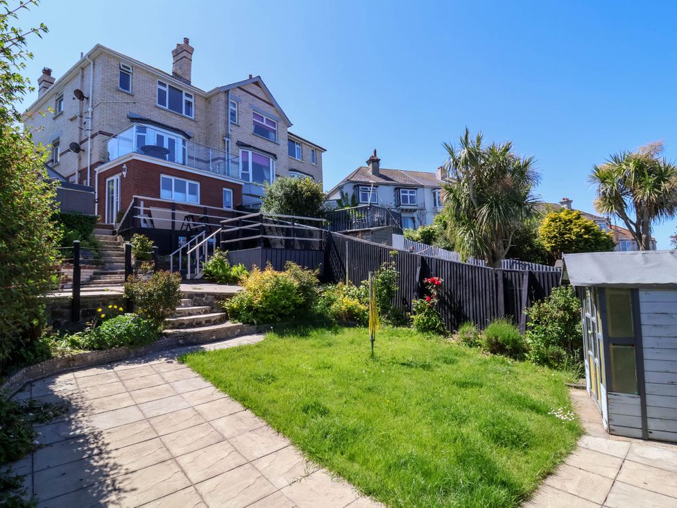 A backyard with grass garden shed stone steps and a large house in the background at Combe View in Ilfracombe