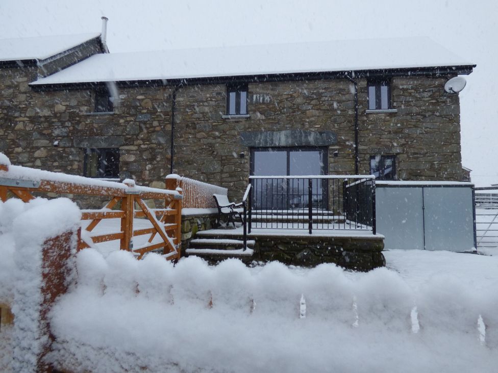 A house covered in snow with a railing and steps at Y Stabl in Cerrigydrudion