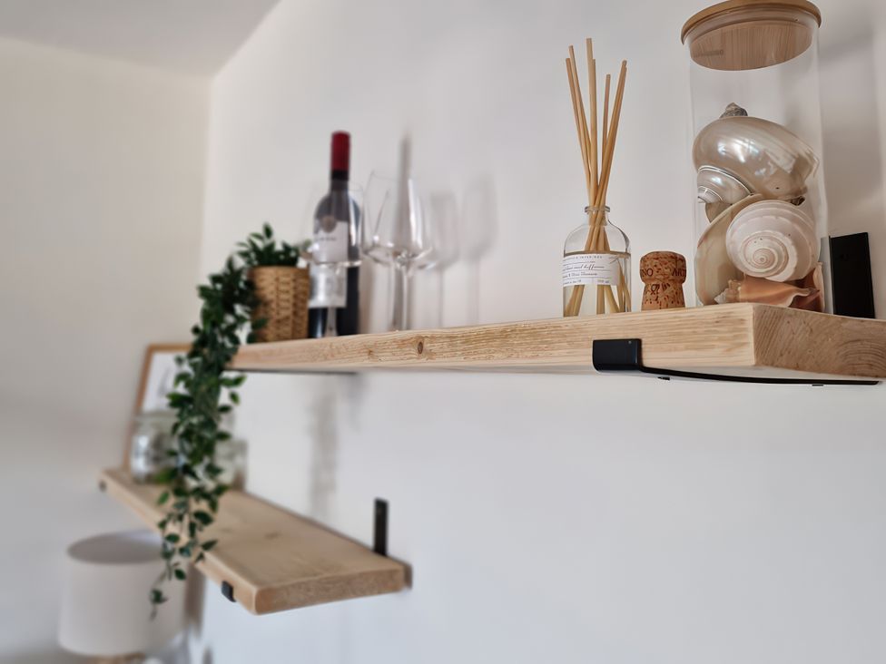 A shelf with wine bottle, glasses, decorative items and seashells at Plas Darien Apartment 7, Trearddur Bay