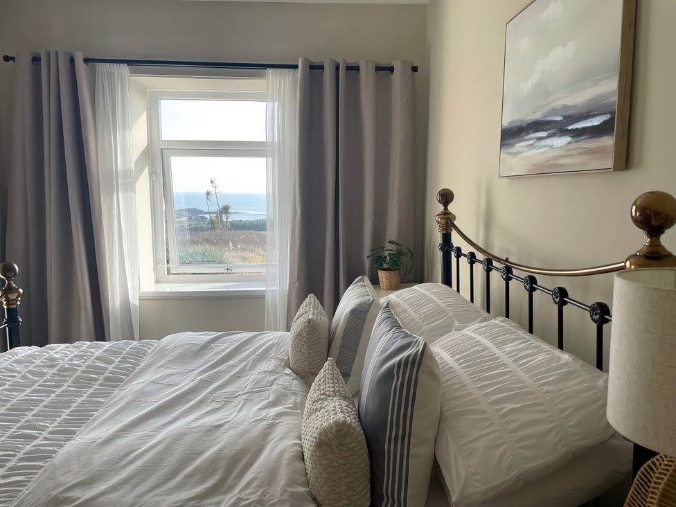 A bedroom with a bed and window overlooking the sea at Plas Darien Apartment 7 Trearddur Bay