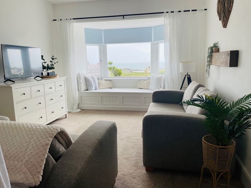 A living room with a television, sofa, and window seat at Plas Darien Apartment 7 in Trearddur Bay