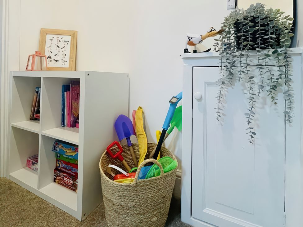 A storage area with a shelf of books and a basket of toys at Plas Darien Apartment 7 in Trearddur Bay
