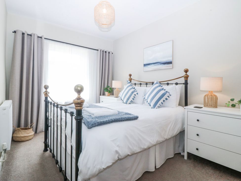 A bedroom with a bed, bedside table, and window at No.7 Plas Darien in Trearddur Bay
