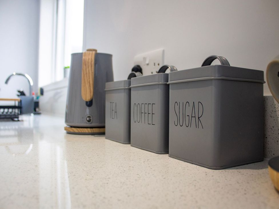 A kitchen countertop with a kettle and canisters for tea, coffee, and sugar at Crannoch Self Catering in Buckie