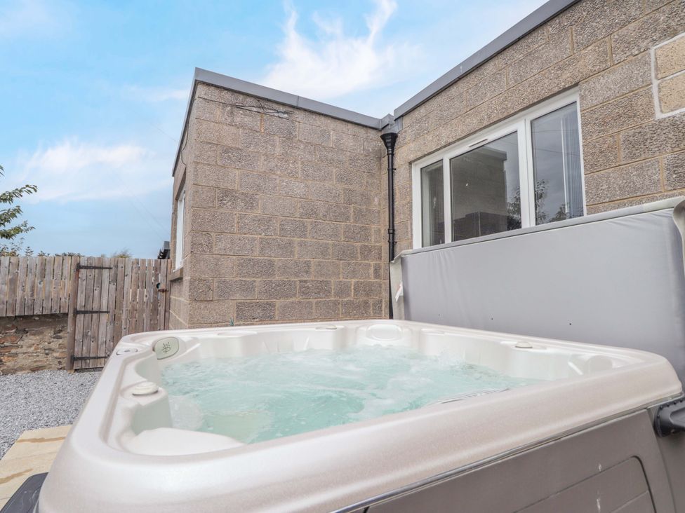 A hot tub next to a stone wall and window at Crannoch Self Catering in Cullen