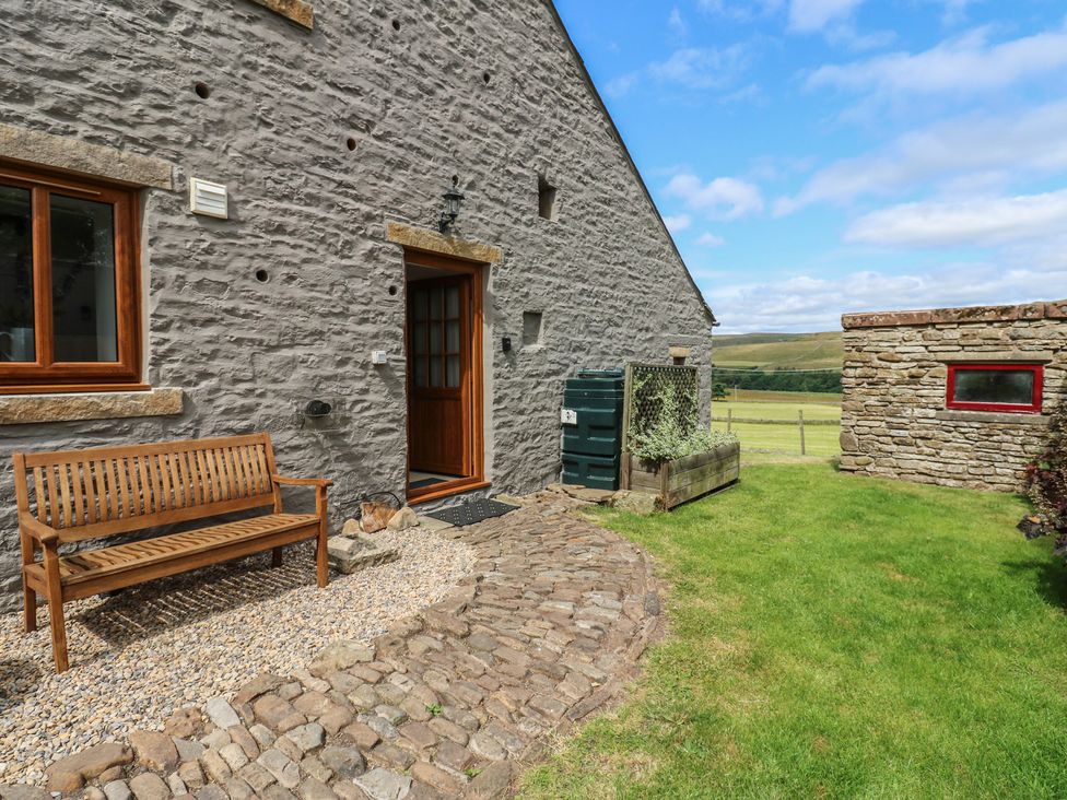 An outdoor area with a stone wall and wooden bench at Middlefell View Cottage Alston