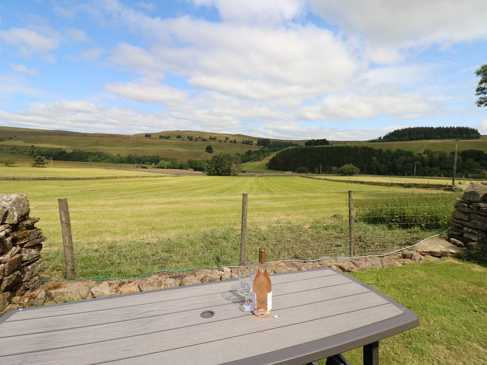 A table with a wine bottle and glasses overlooking a field at Middlefell View Cottage in Alston
