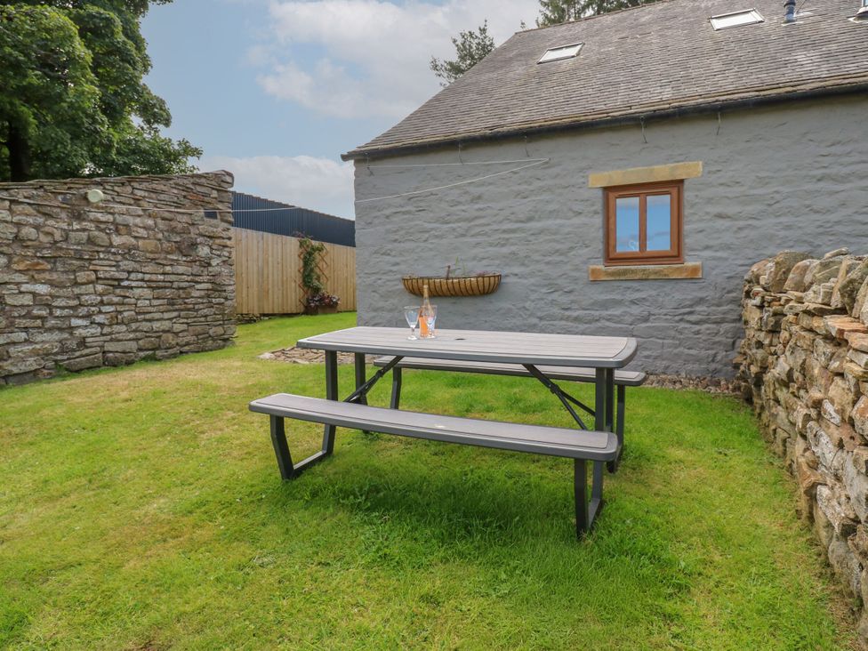 A picnic table with glass bottles next to a stone wall at Middlefell View Cottage in Alston