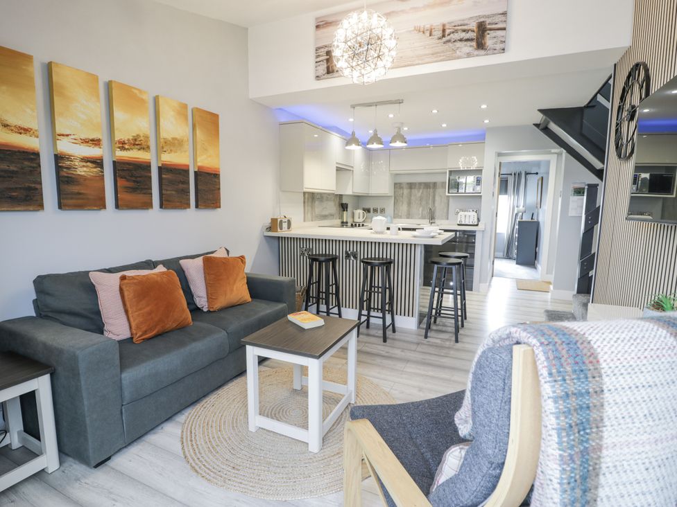 A living room with a sofa, coffee table, and kitchen area at Harbwr Hideaway in Porthmadog