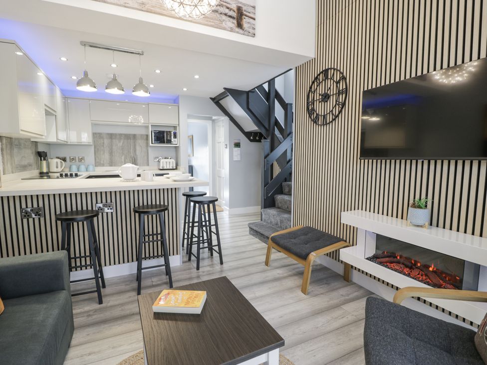 A living room with a kitchen area and a staircase at Harbwr Hideaway in Porthmadog