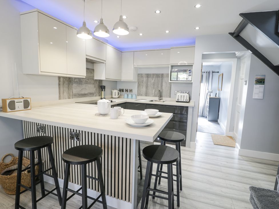 A kitchen with bar stools and modern appliances at Harbwr Hideaway in Porthmadog
