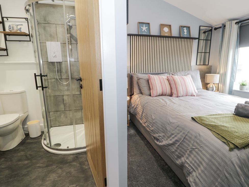 A bathroom with a shower and toilet adjacent to a bedroom with a bed at Harbwr Hideaway, Porthmadog