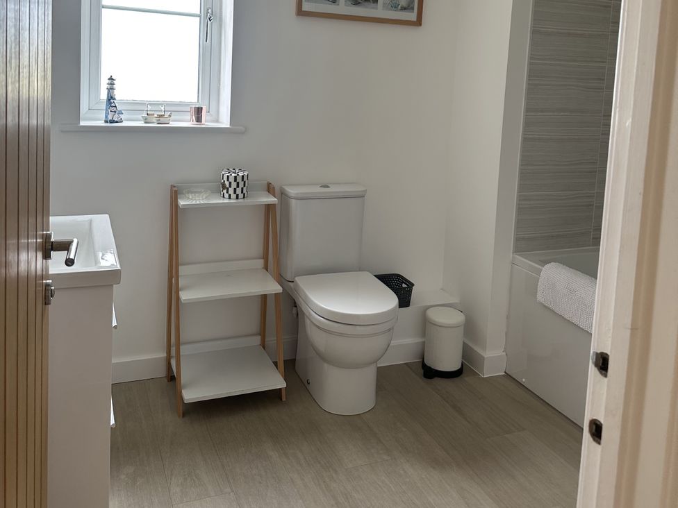 A bathroom with a toilet, shelf, and bathtub at 9 Coastguard Cottages in Woolacombe