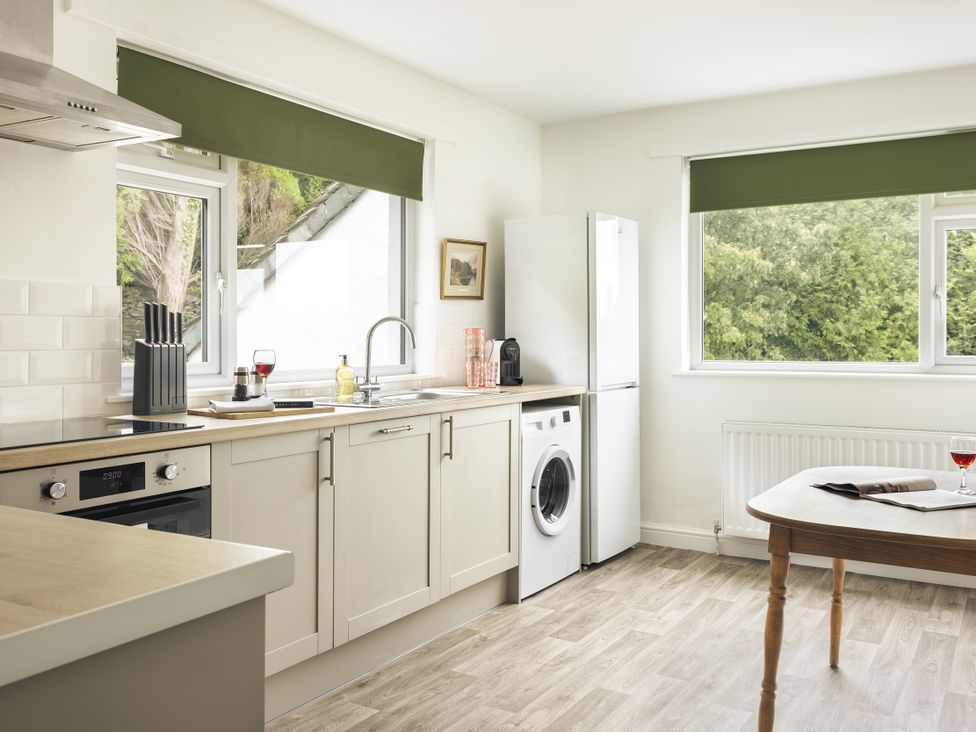 A kitchen with a sink, fridge, washing machine, and kitchen counter at Tethers End in Lindeth near Bowness-On-Windermere