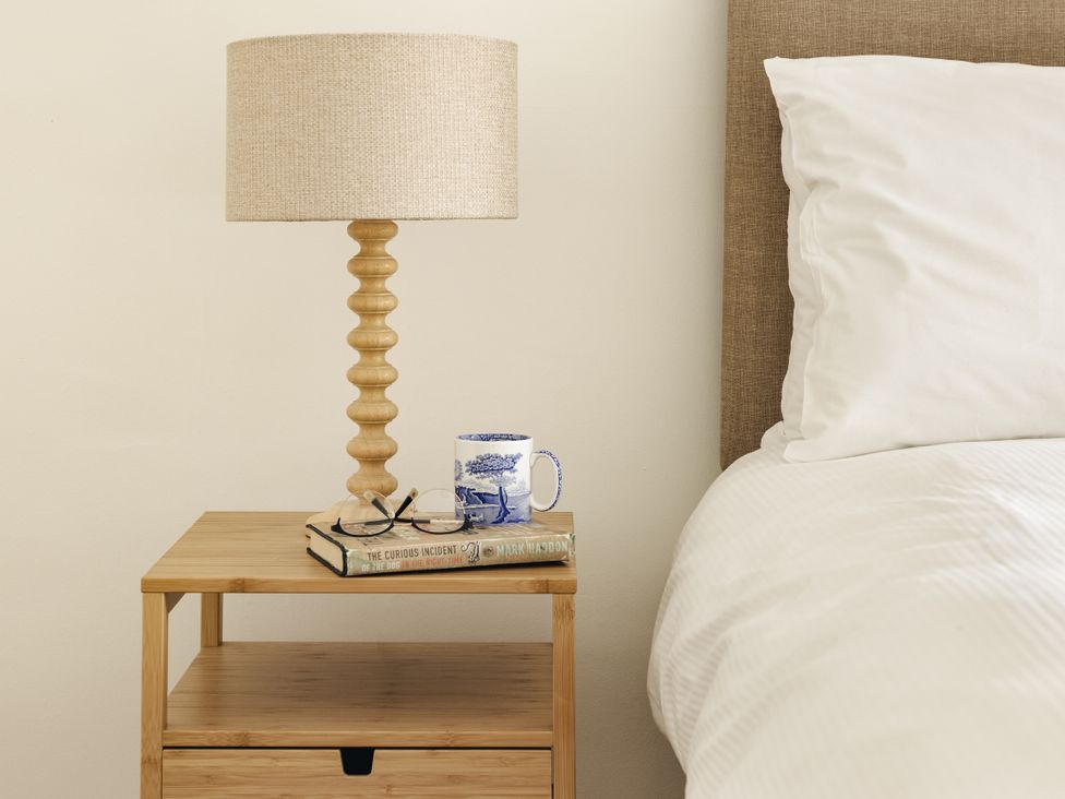 A bedroom with a nightstand, lamp, mug, book, and eyeglasses at Tethers End in Lindeth near Bowness-On-Windermere