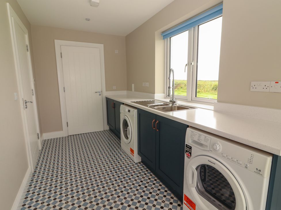 A utility room with a washer, dryer, and sink at Carrowmore North in Doonbeg, County Clare