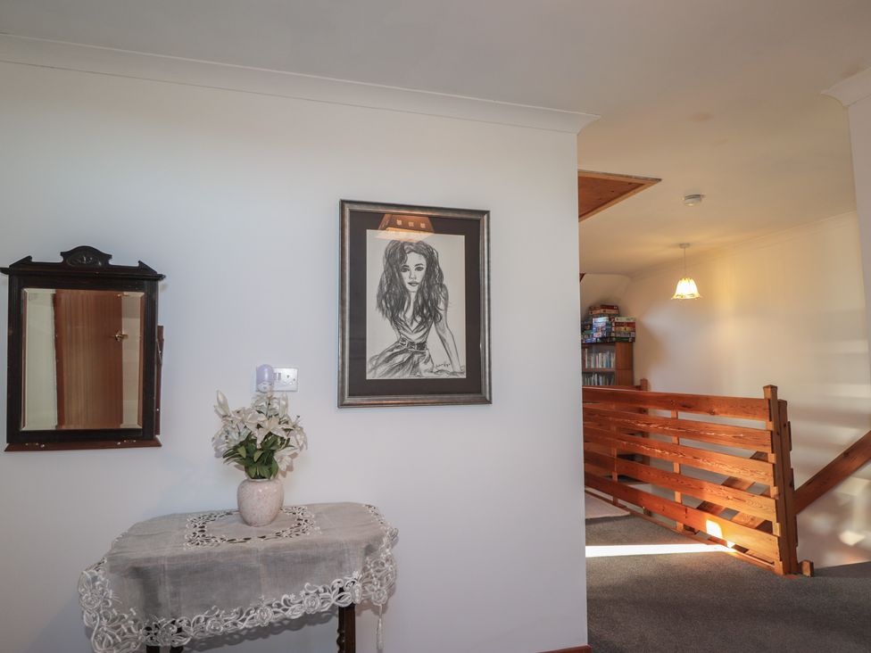 A hallway with a mirror, portrait, table, and flowers at Arnaval in Carbost