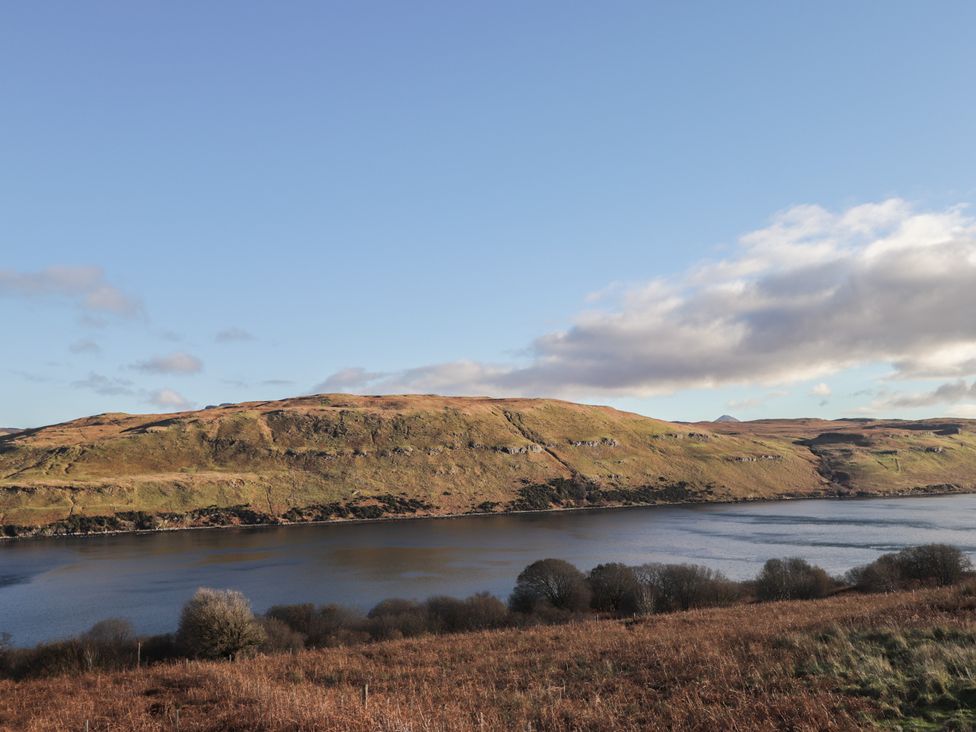 A hill beside a lake with grass and bushes at Arnaval in Carbost