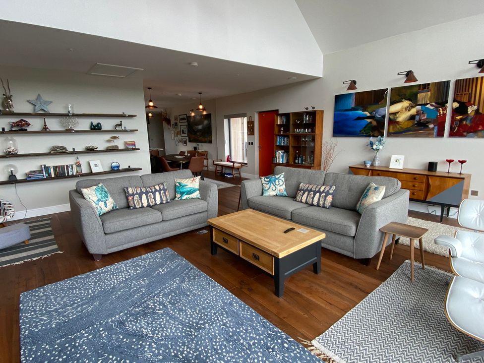 A living room with two sofas, a coffee table, and shelves at Woodcroft in Pwllheli