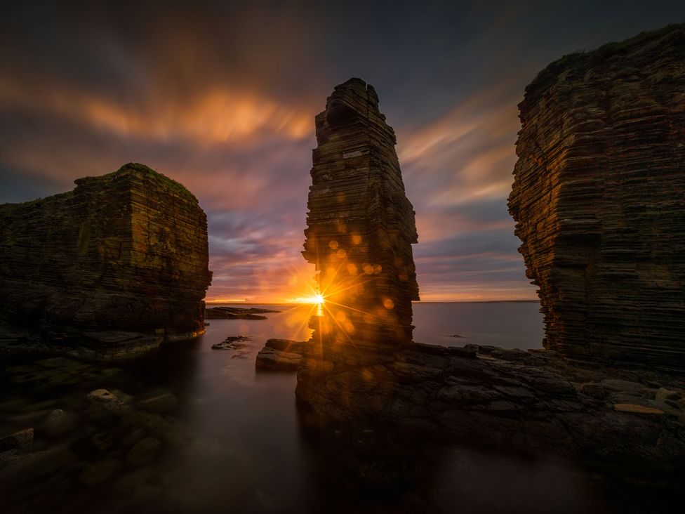 A scenic view featuring rock formations and a sunset at a coastal location