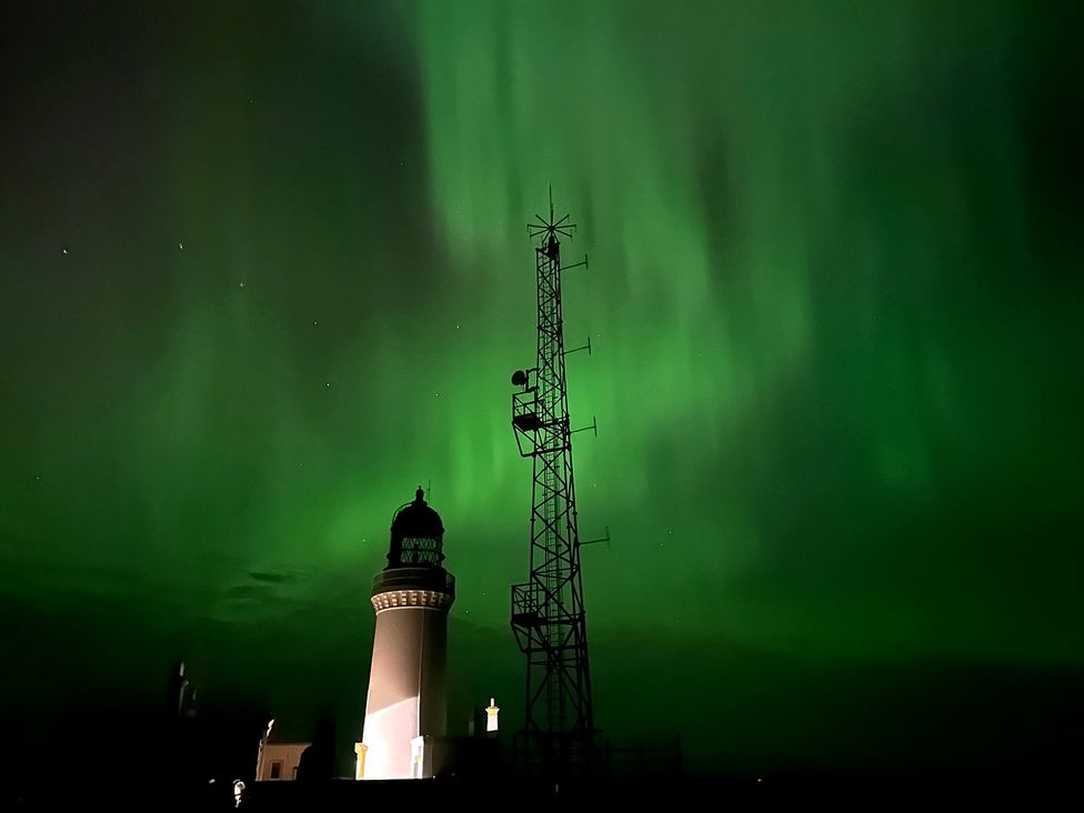 A lighthouse and communication tower under northern lights at The Lighthouse Keepers Cabin Noss Head near Wick Caithness