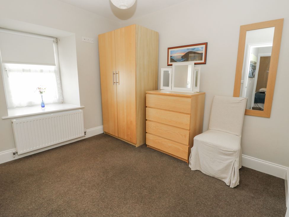 A bedroom with a wardrobe, chest of drawers, chair, and mirror at Station Hall in Cilgerran