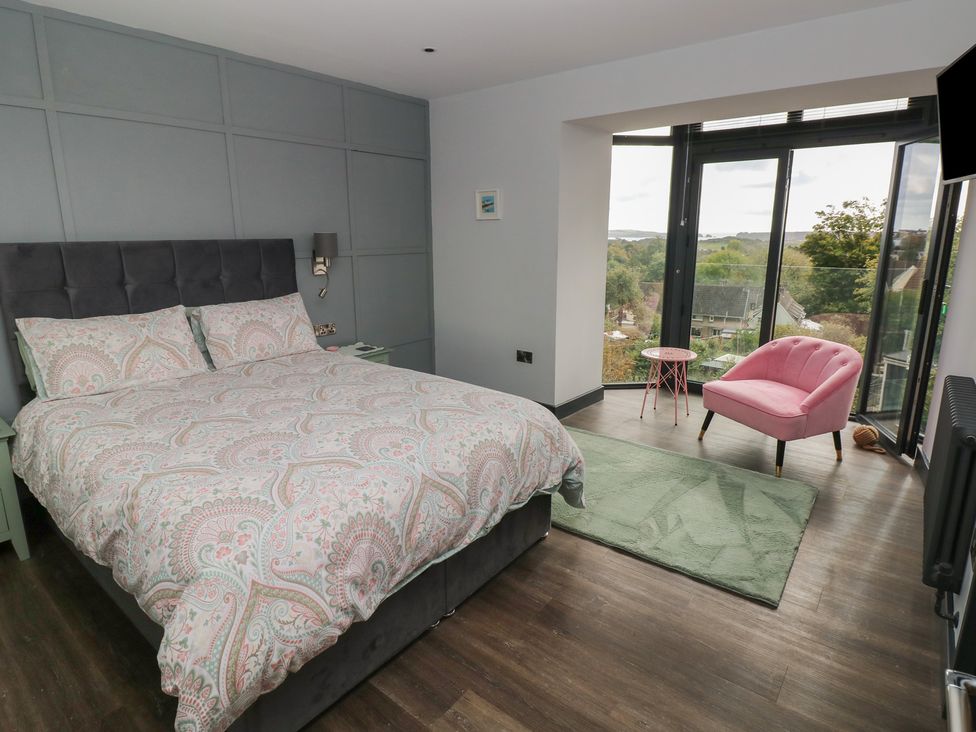 A bedroom with a bed and pink chair at 9 Brython Place in Tenby