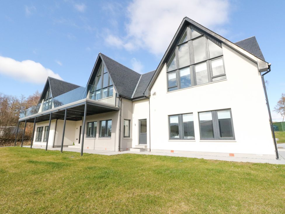A modern two story house with triangular roof windows and a balcony overlooking a grassy yard at Macgregor Ranch in Achnabobane near Spean Bridge