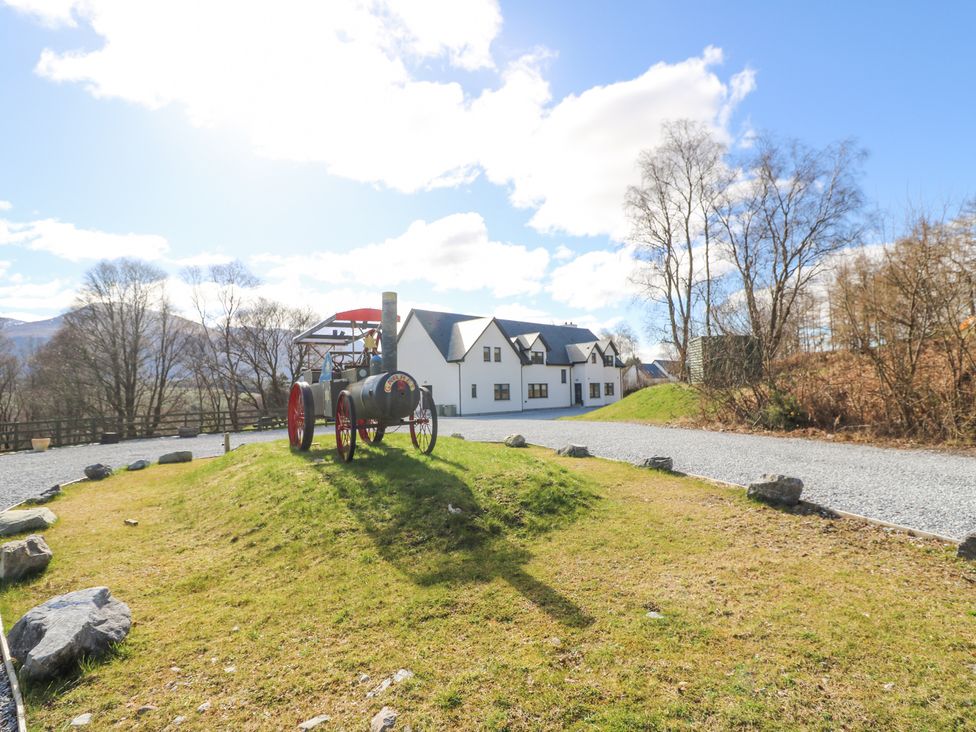 An outdoor scene with a vintage steam tractor on a grassy mound and a white house in the background at Macgregor Ranch in Achnabobane near Spean Bridge