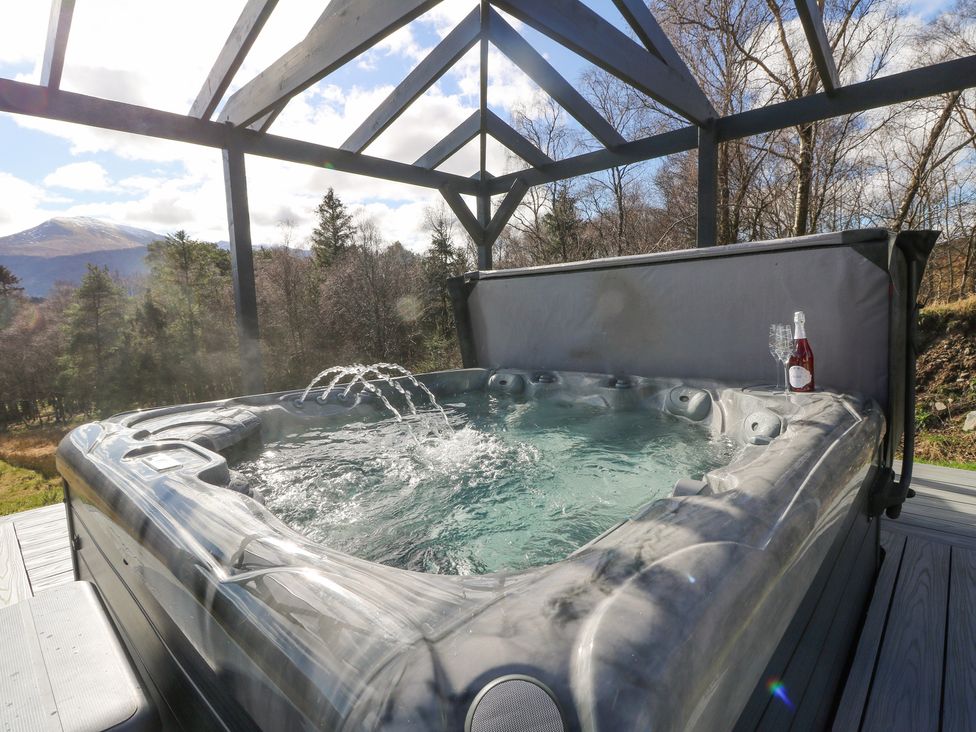 An outdoor hot tub with water jets under a wooden pergola surrounded by trees and mountains at Macgregor Ranch in Achnabobane near Spean Bridge
