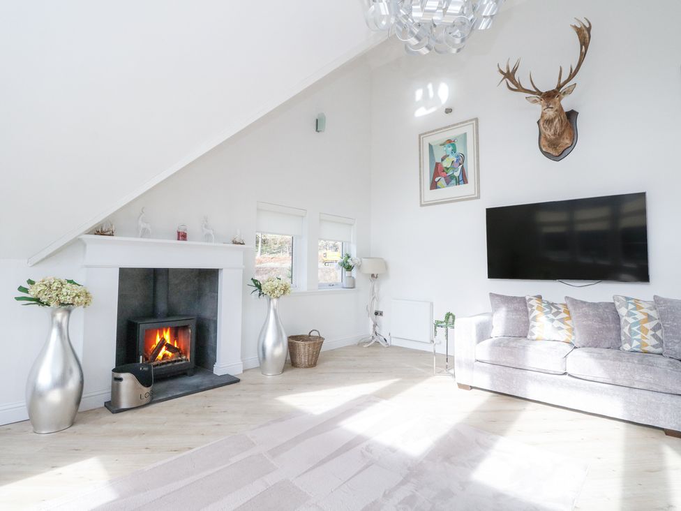 A living room with a fireplace a sofa a mounted deer head and a large TV at Macgregor Ranch in Achnabobane near Spean Bridge
