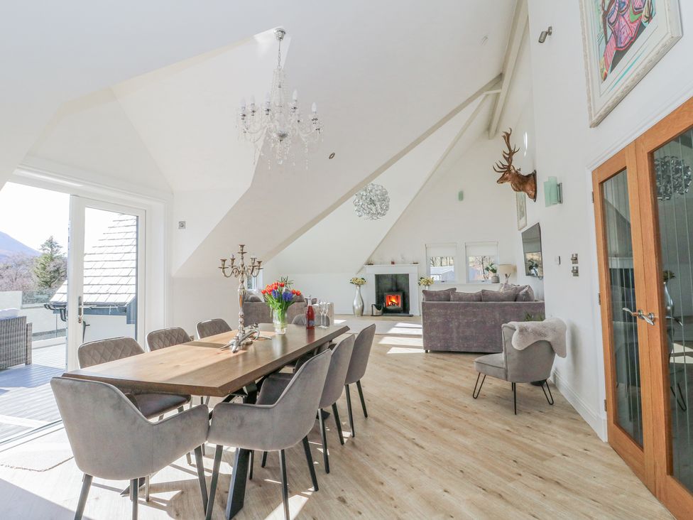 A dining area with a wooden table and chairs next to a living room with sofas and a fireplace at Macgregor Ranch in Achnabobane near Spean Bridge