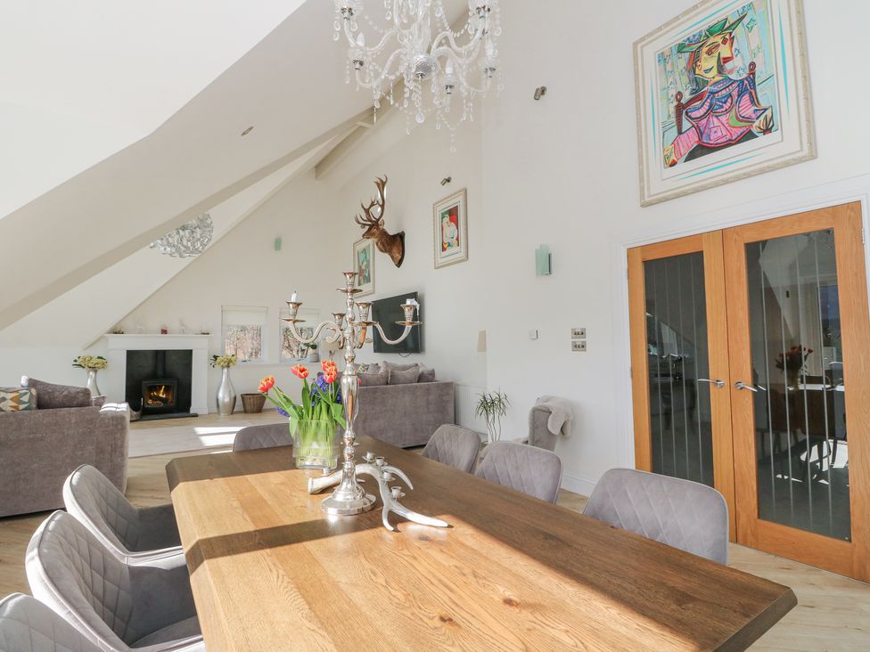 A dining room with a wooden table and gray chairs next to a living area with sofas and a fireplace at Macgregor Ranch in Achnabobane near Spean Bridge