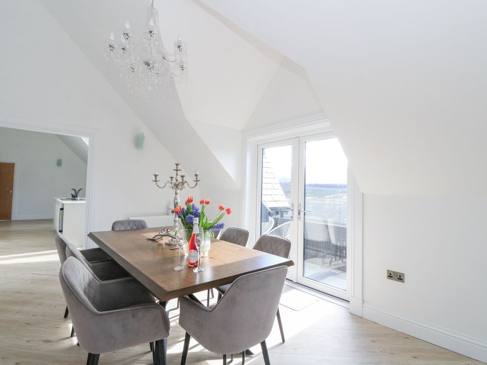 A dining area with a wooden table surrounded by six grey chairs a chandelier above and glass doors leading outside at Macgregor Ranch in Achnabobane near Spean Bridge