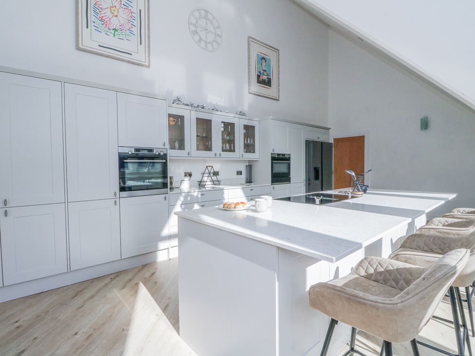 A kitchen with white cabinets an island with a cooktop stools a clock and framed artwork on the walls at Macgregor Ranch Achnabobane near Spean Bridge