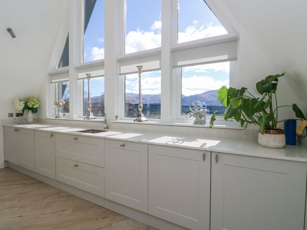 A kitchen with white cabinets a sink large windows with mountain views and plants on the countertop at Macgregor Ranch in Achnabobane near Spean Bridge