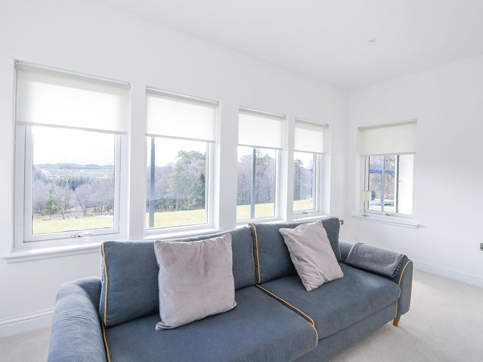 A living room with a blue sofa and grey cushions in front of four windows with white blinds at Macgregor Ranch in Achnabobane near Spean Bridge