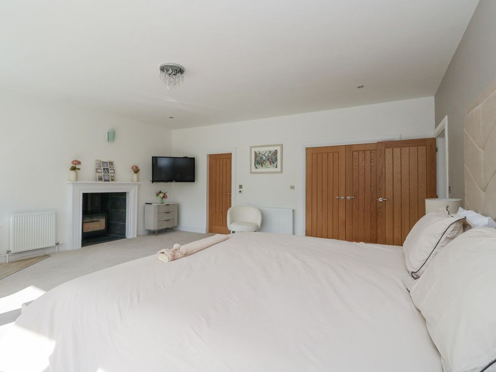 A bedroom with a bed a fireplace a television a chair wooden doors and a side table at Macgregor Ranch in Achnabobane near Spean Bridge