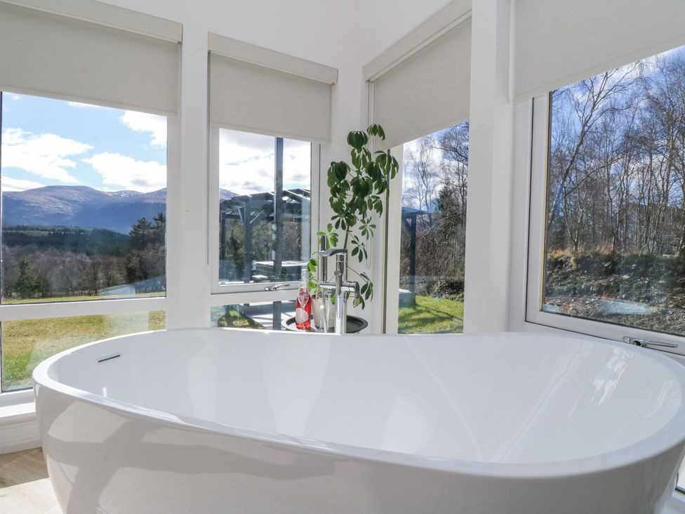 A bathroom with a white freestanding bathtub near large windows showing an outdoor landscape at Macgregor Ranch in Achnabobane near Spean Bridge