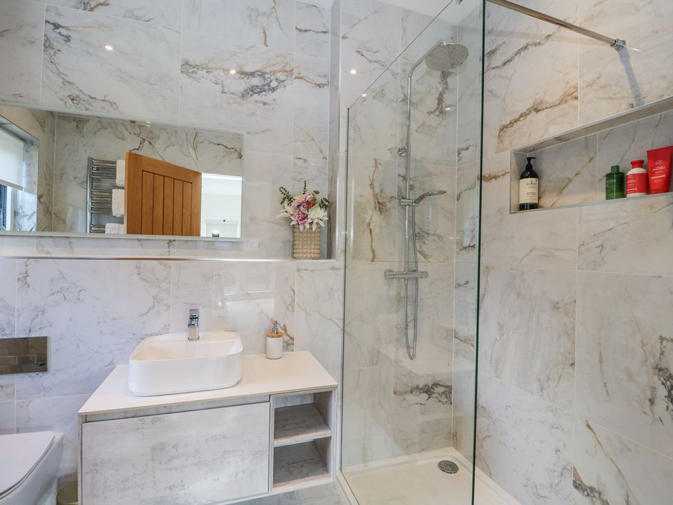 A bathroom with a shower enclosure sink with faucet a mirror and toiletries at Macgregor Ranch in Achnabobane near Spean Bridge