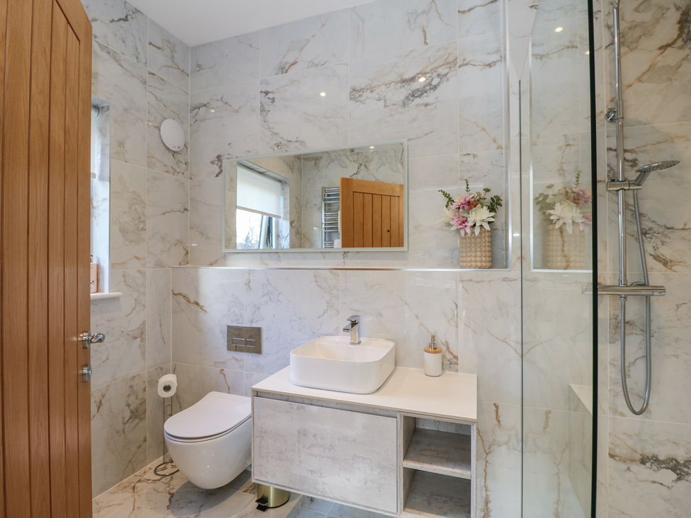A bathroom with a toilet sink mirror shower and flowers on the counter at Macgregor Ranch in Achnabobane near Spean Bridge