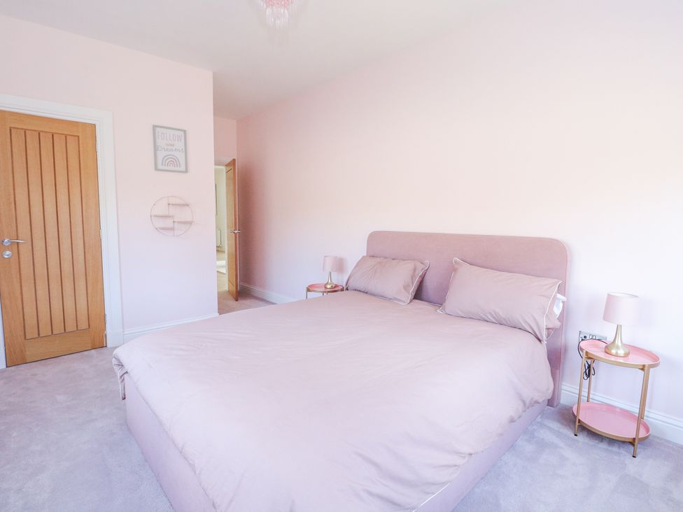 A bedroom with a double bed two bedside tables and lamps a wooden door and light pink walls at Macgregor Ranch in Achnabobane near Spean Bridge