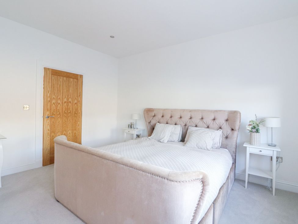 A bedroom with a beige upholstered bed and white nightstands near Macgregor Ranch in Achnabobane near Spean Bridge