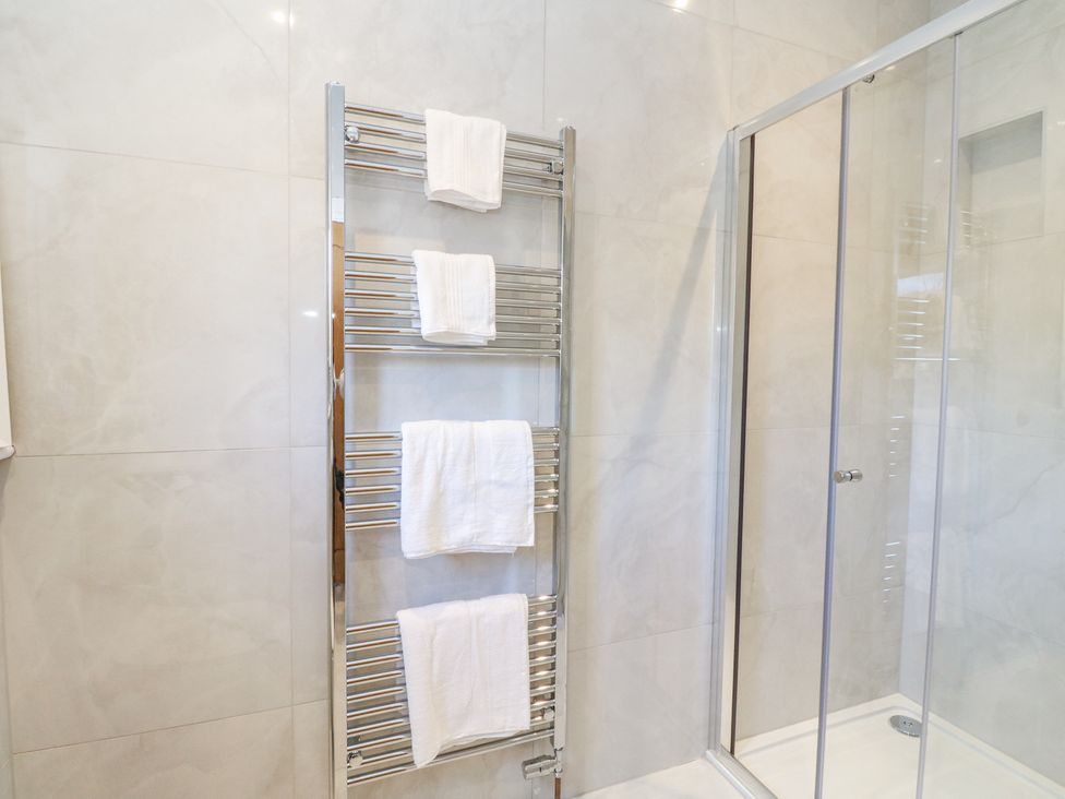 A bathroom with a chrome towel rack holding white towels next to a glass shower enclosure at Macgregor Ranch in Achnabobane near Spean Bridge