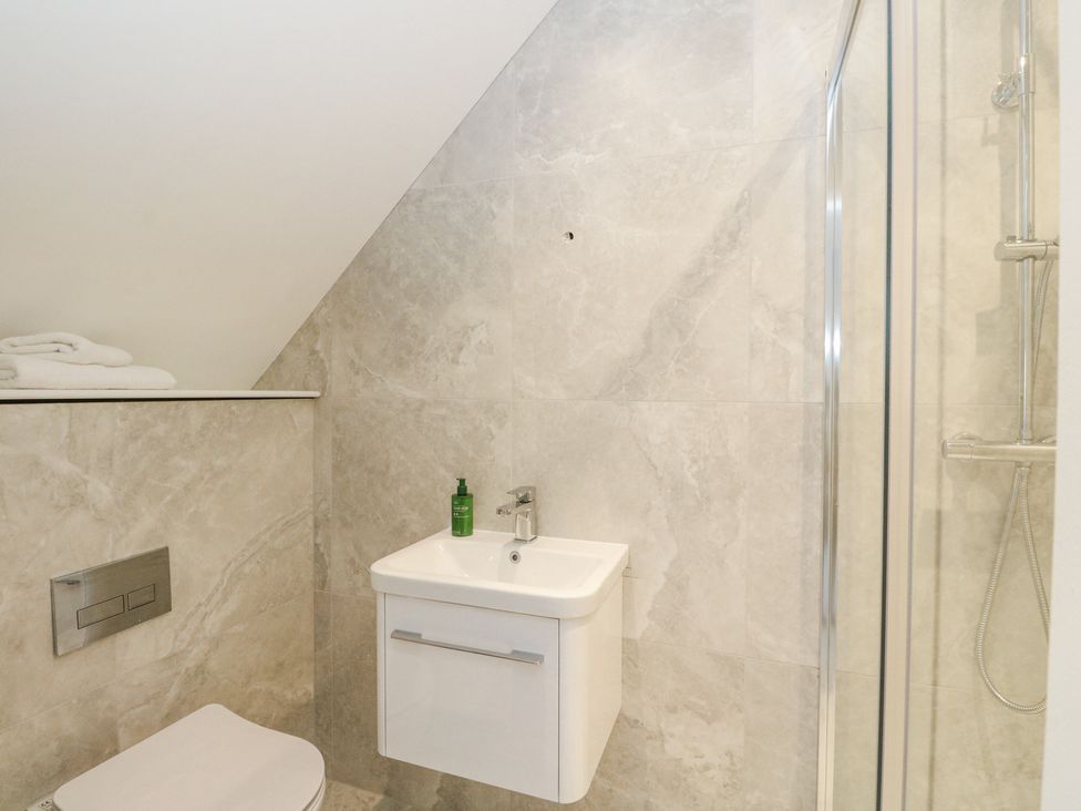 A bathroom with a wall-mounted toilet sink with a green bottle and a shower with glass door at Macgregor Ranch in Achnabobane near Spean Bridge