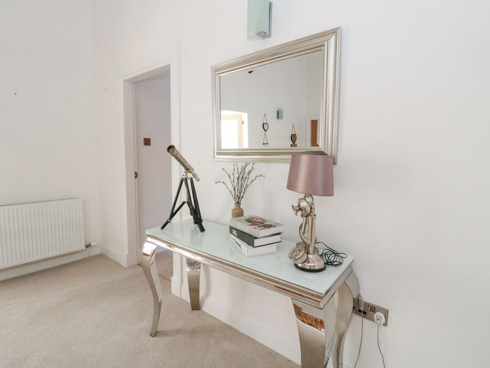 A hallway with a metallic console table holding a telescope lamp books and a vase under a wall mirror at Macgregor Ranch in Achnabobane near Spean Bridge