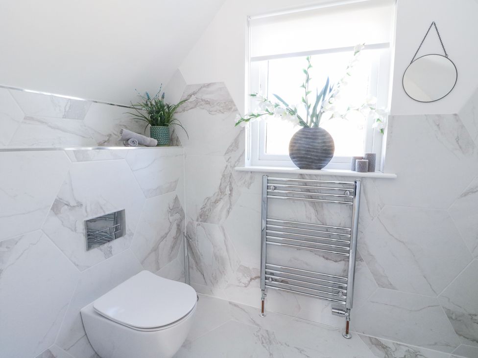 A bathroom with a wall mounted toilet a towel warmer a window with flowers in a vase and a small round mirror on the wall at Macgregor Ranch in Achnabobane near Spean Bridge
