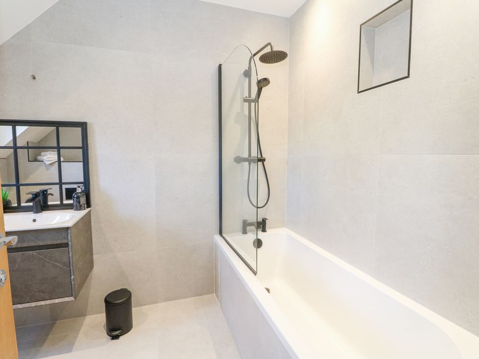 A bathroom with a bathtub shower combination a sink with mirror and a small bin at Macgregor Ranch in Achnabobane near Spean Bridge